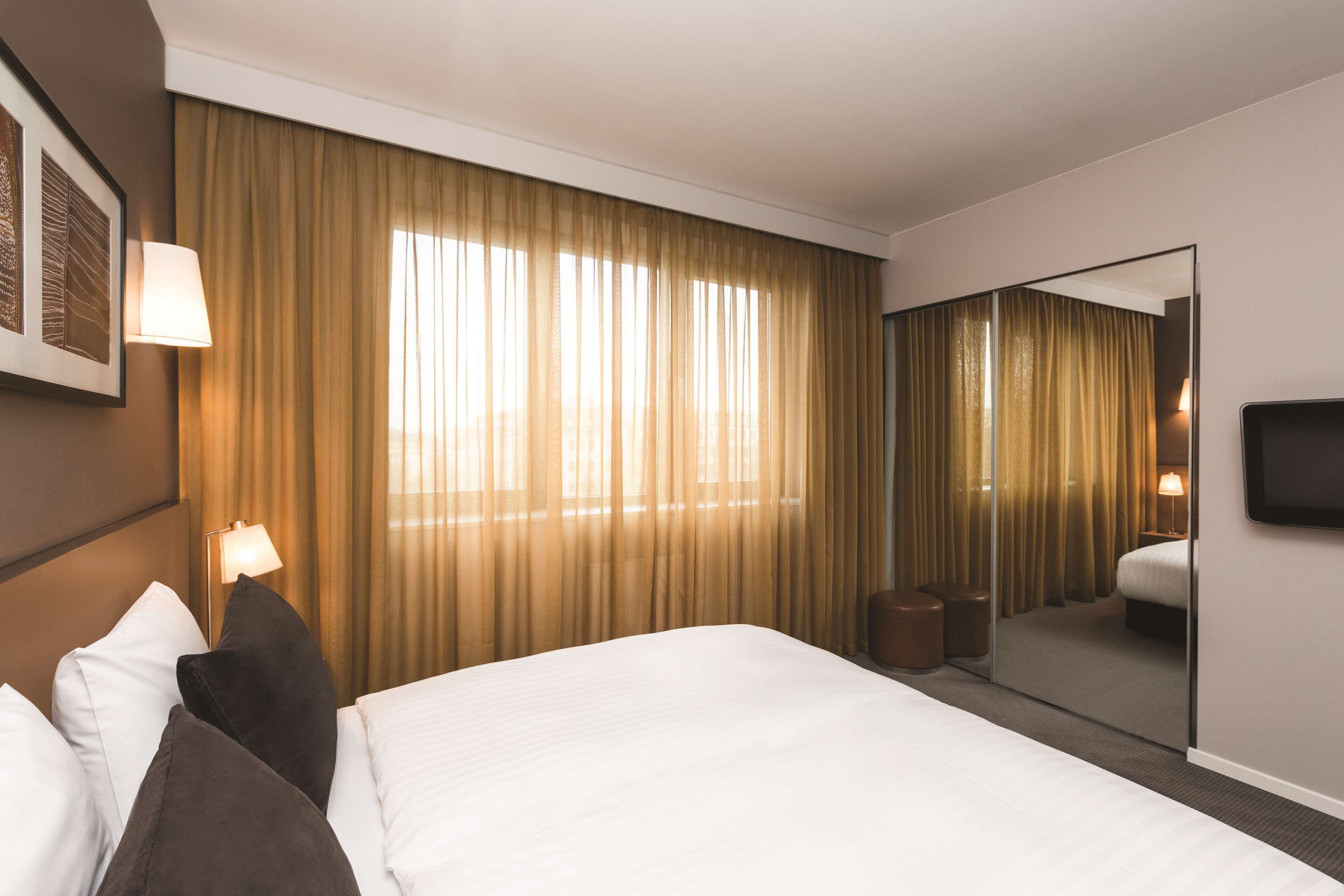 A hotel room with a large bed, a bedside lamp, a mirror, and a window with curtains.