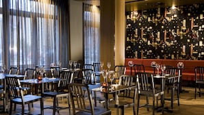 A restaurant with tables set for dining, featuring a modern interior with a patterned wall and large windows with curtains. - Adina Apartment Hotel Berlin Mitte (Berlin)
