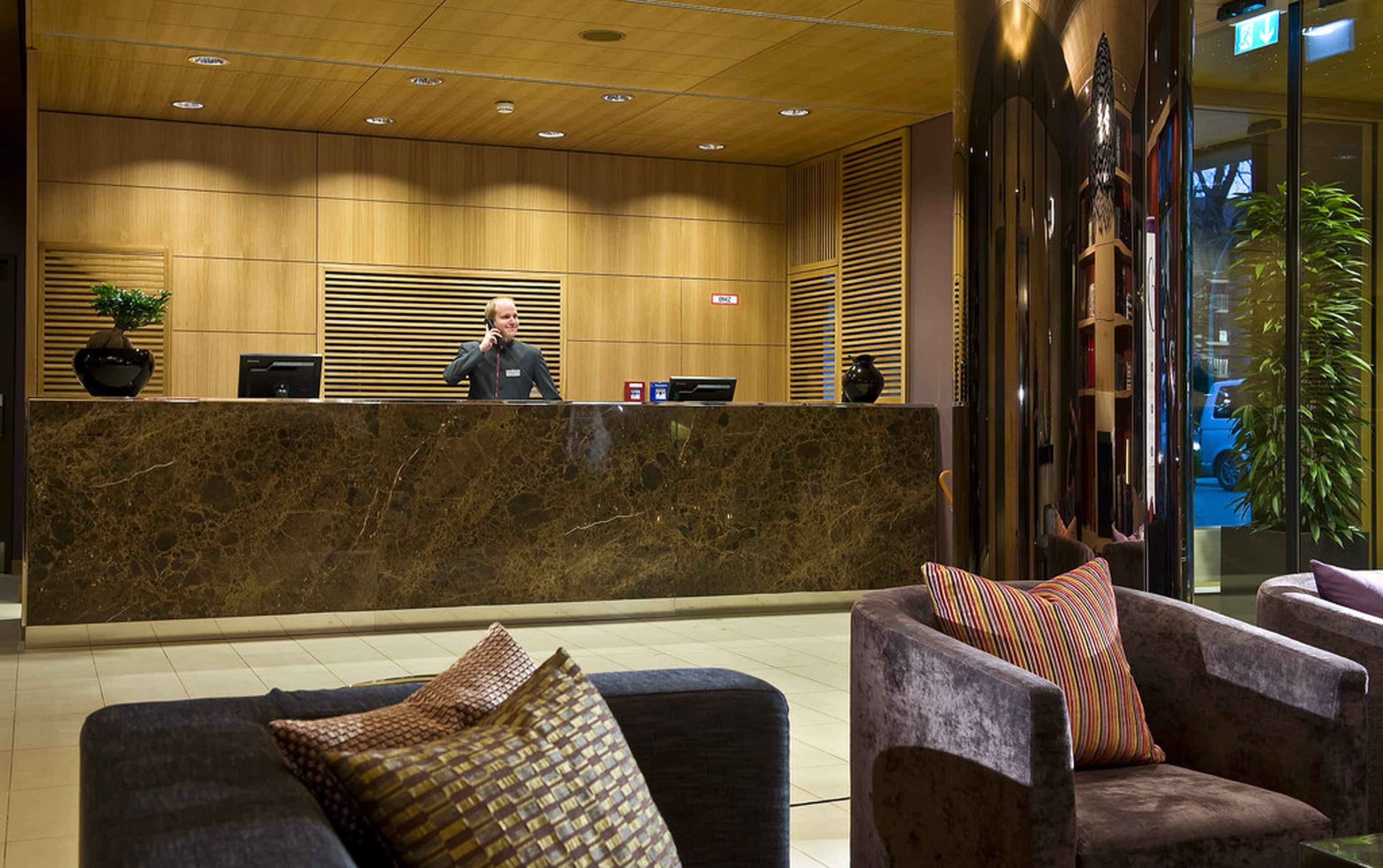 A reception area with a marble counter, wooden paneling, and two armchairs with patterned cushions.