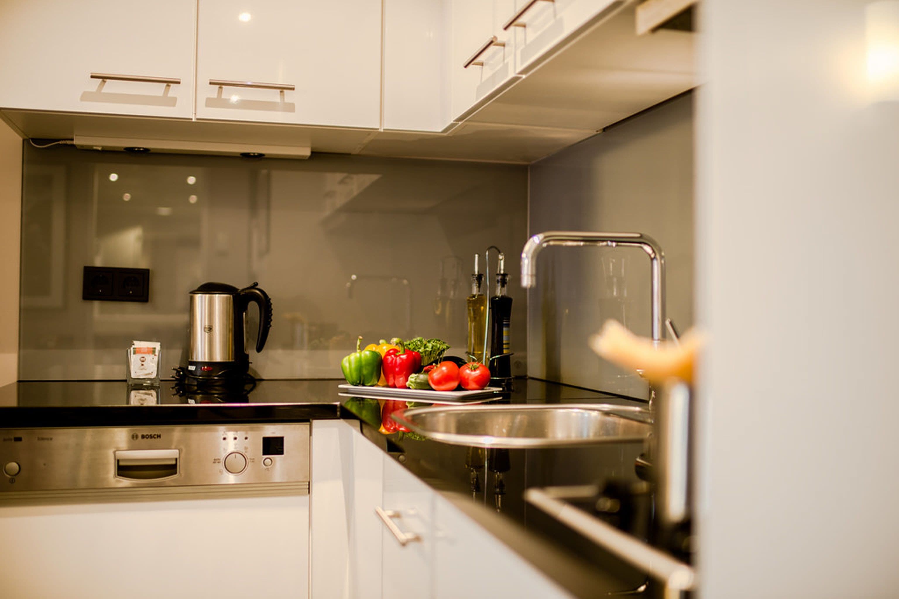 Een moderne keuken met een Bosch vaatwasser, een waterkoker en verse groenten op het aanrecht.