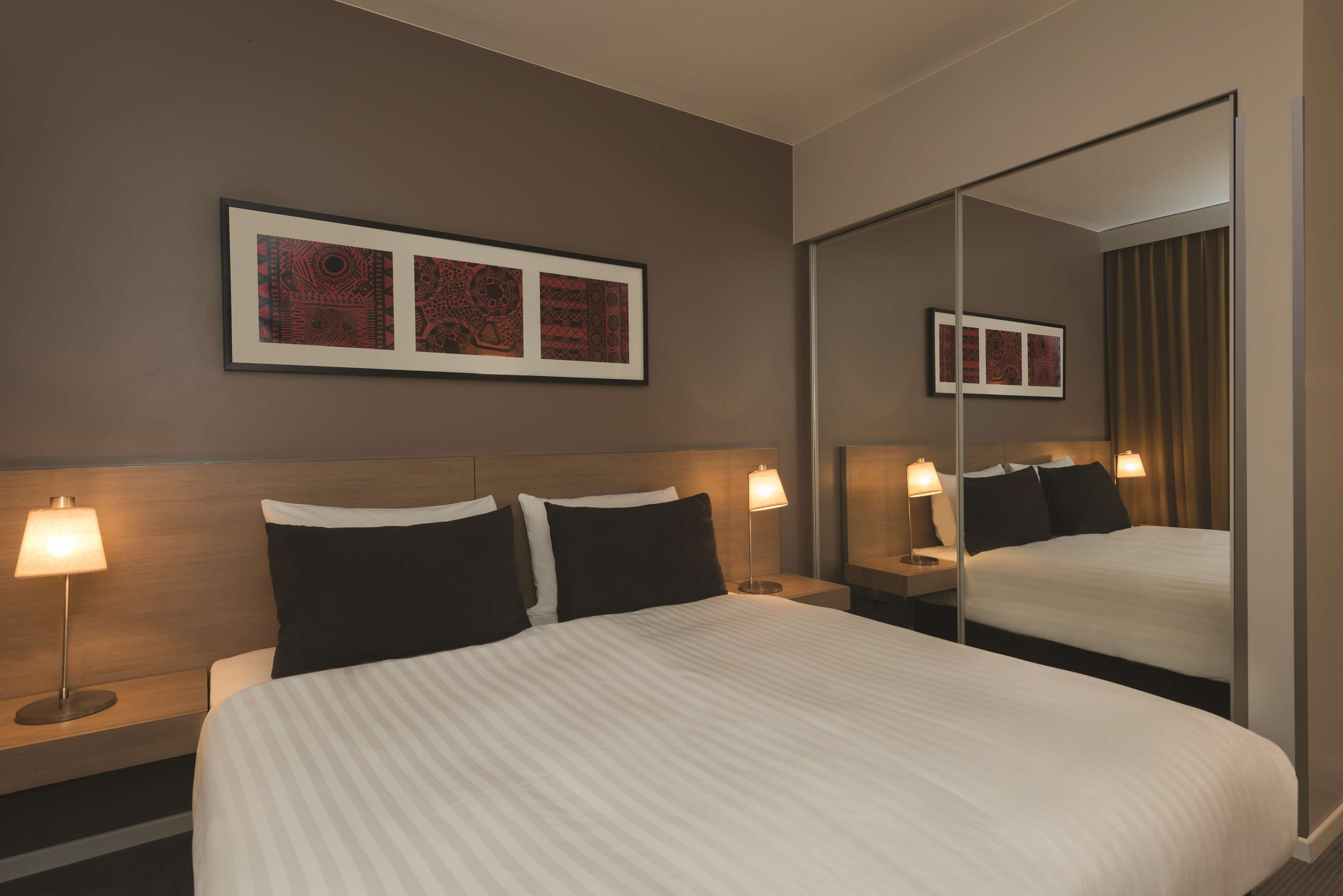 Una habitación de hotel con una cama grande, dos mesitas de noche con lámparas, un espejo montado en la pared y obras de arte enmarcadas.