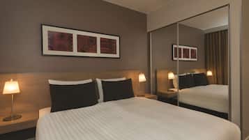Una habitación de hotel con una cama grande, dos mesitas de noche con lámparas, un espejo montado en la pared y obras de arte enmarcadas.