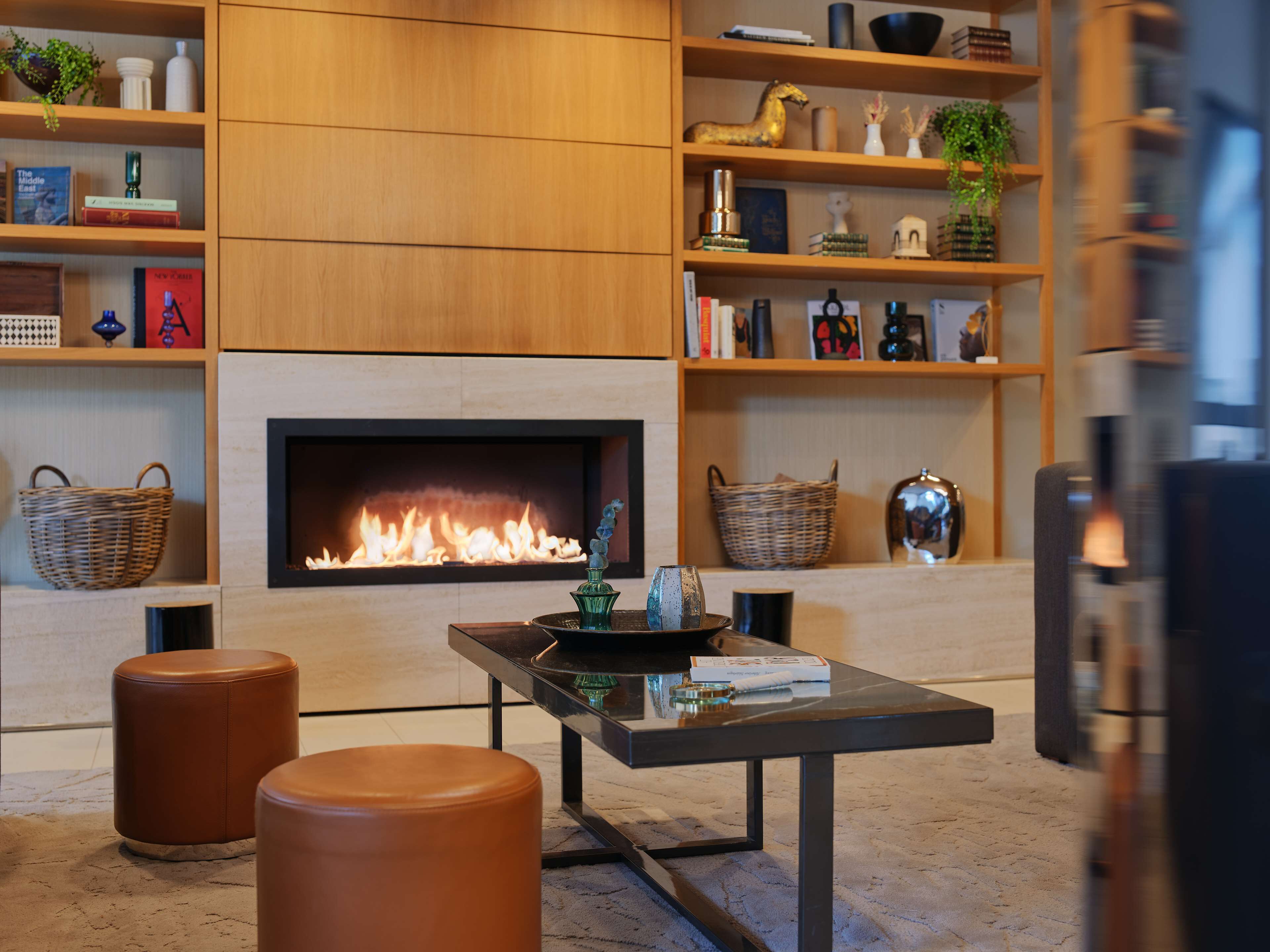 A modern living room with a fireplace, leather ottomans, and shelves with books and decorative items.