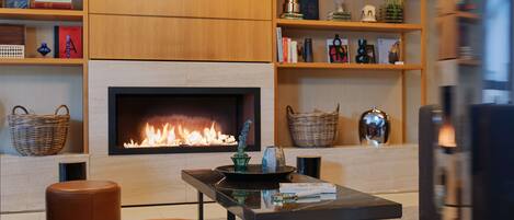 A modern living room with a fireplace, leather ottomans, and shelves with books and decorative items.