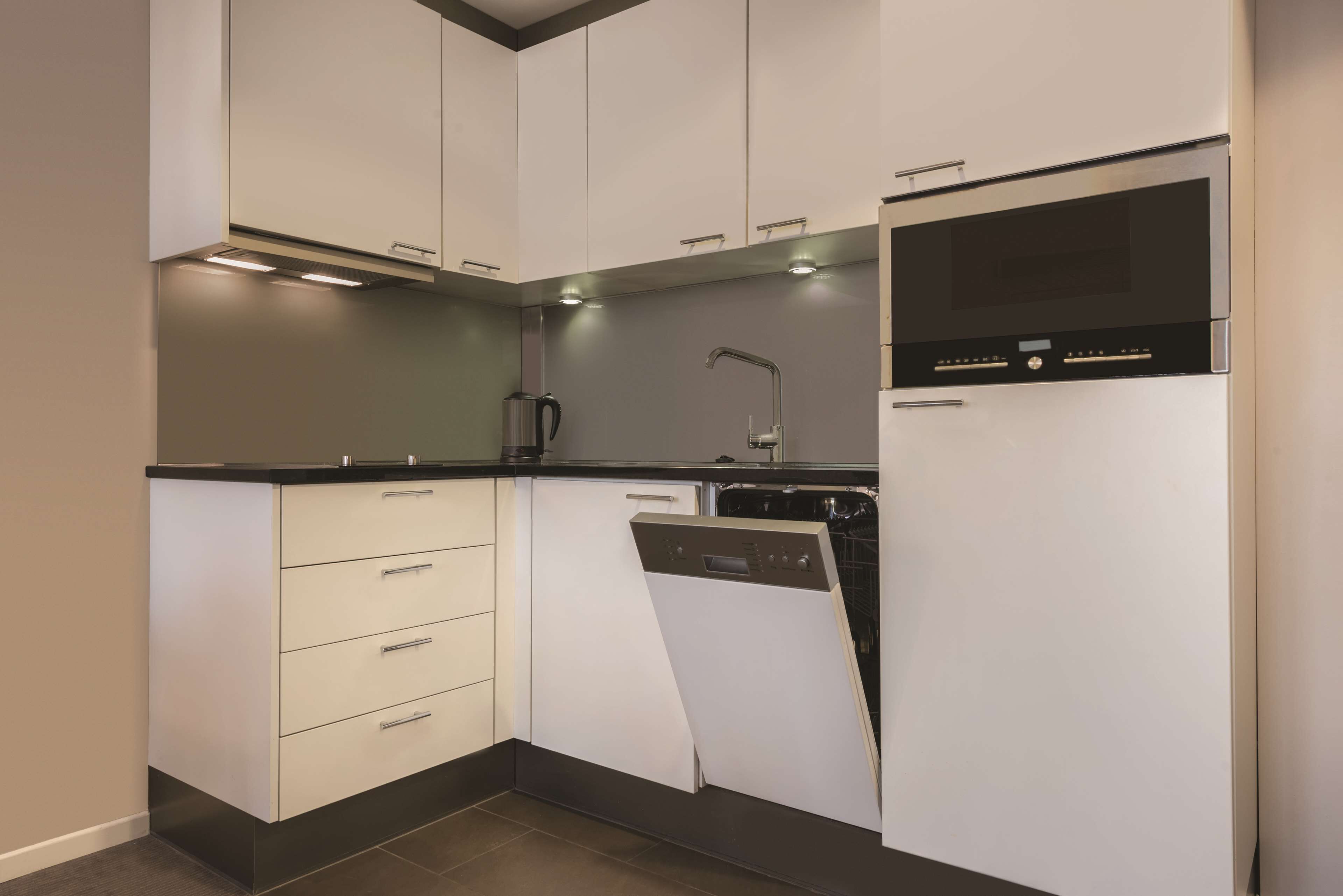 A modern kitchen with white cabinetry, a built-in dishwasher, and a stainless steel oven.