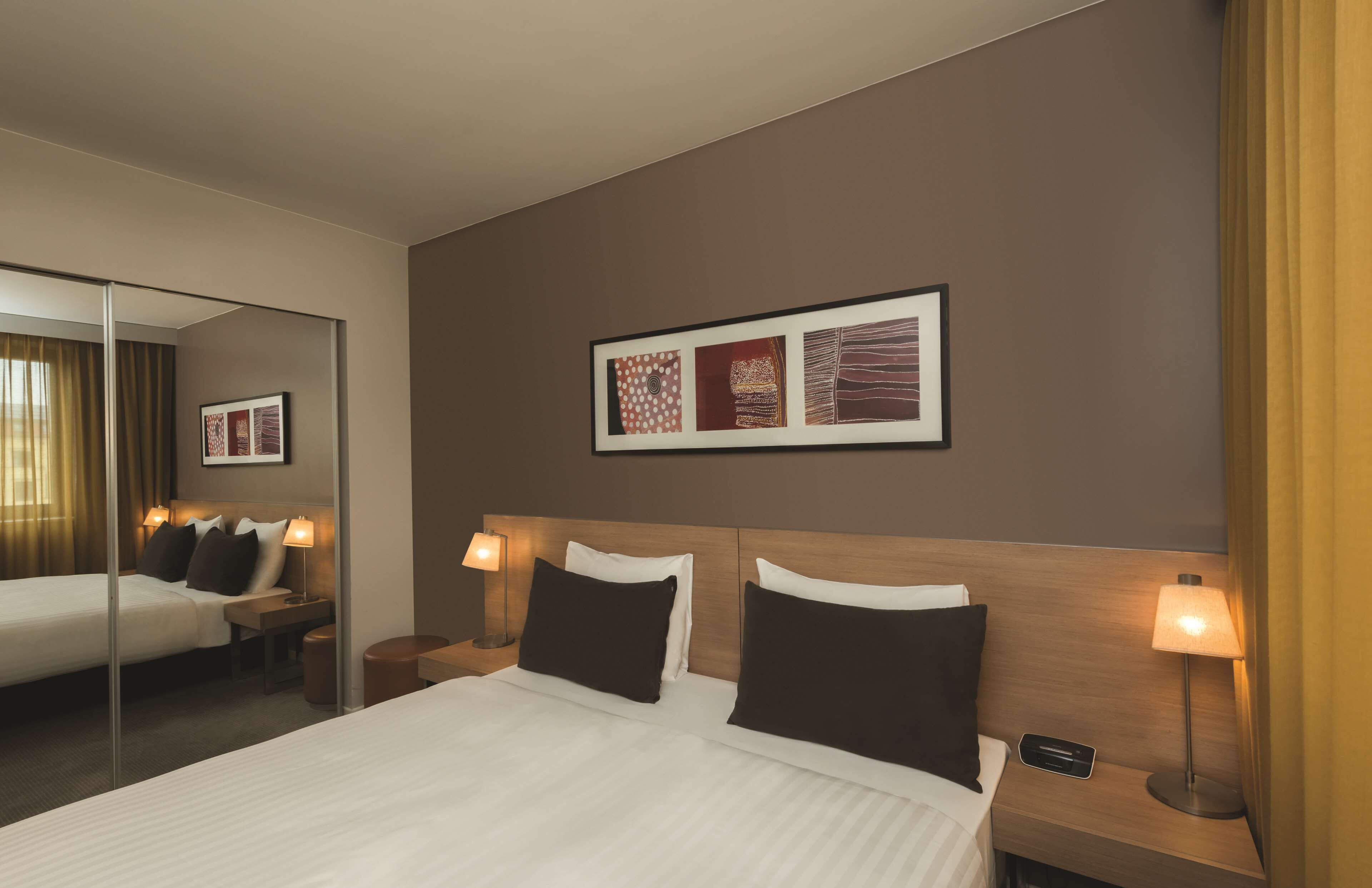A hotel room with a large bed, two bedside tables with lamps, a mirror, and a framed artwork on the wall.