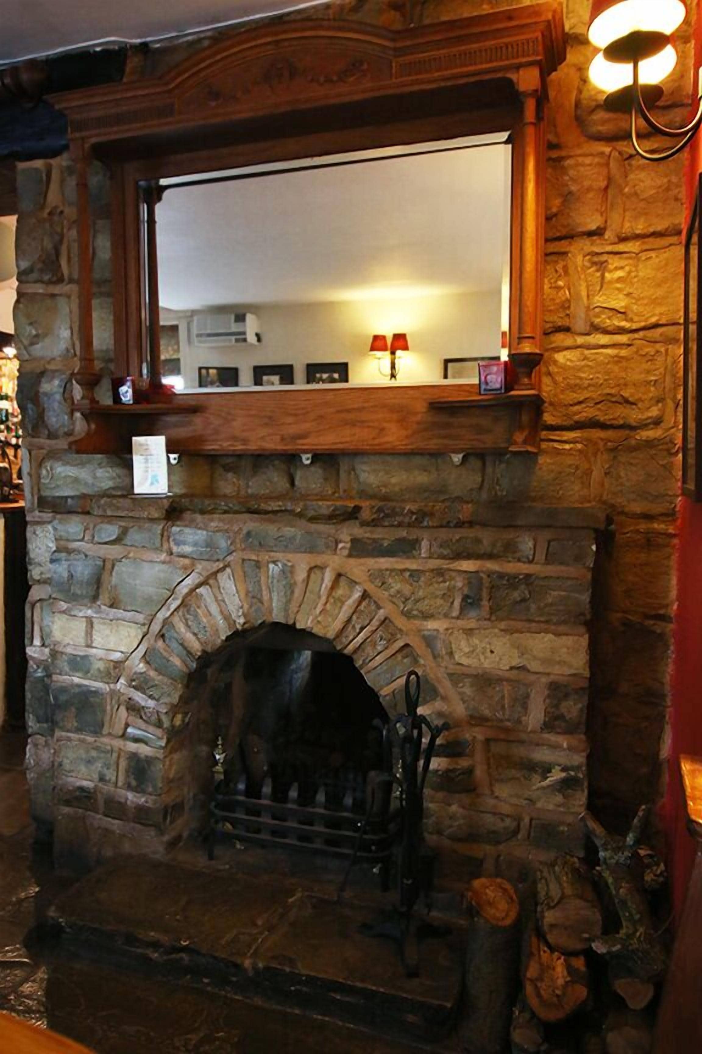 A stone fireplace with a wooden mantel, a mirror above it, and a small shelf with decorative items.