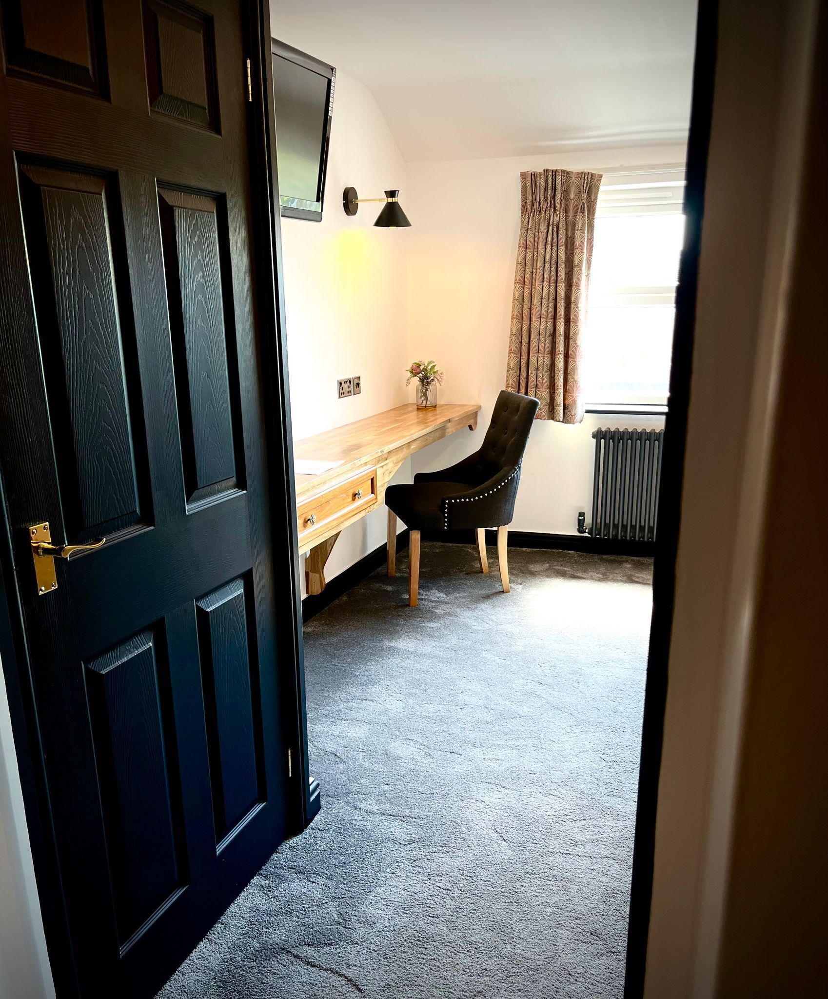 A room with a dark wooden door, a desk with a lamp, a chair, and a radiator.