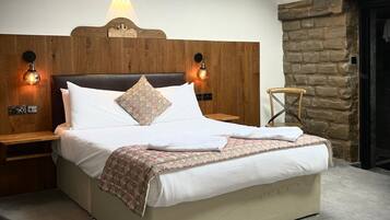 A neatly made bed with a wooden headboard, two bedside lamps, a stone wall, and a skylight above.