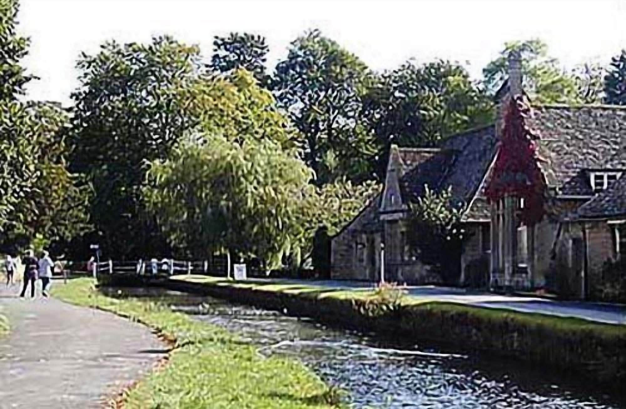 Een voetpad langs de rivier met een gebouw met een rood dak en een standbeeld.