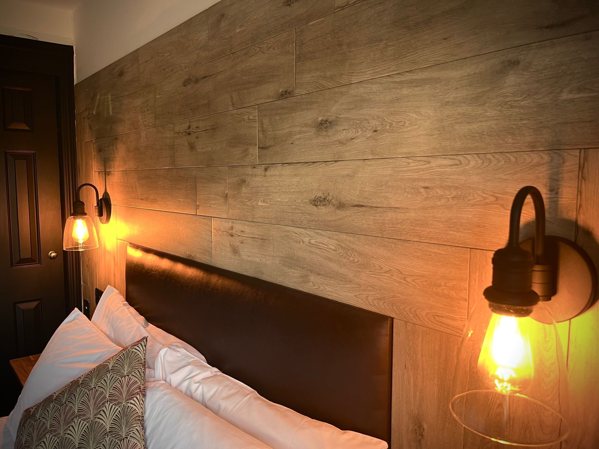 A bedroom with a wooden headboard, two wall-mounted lamps, and a bed with white and patterned pillows.