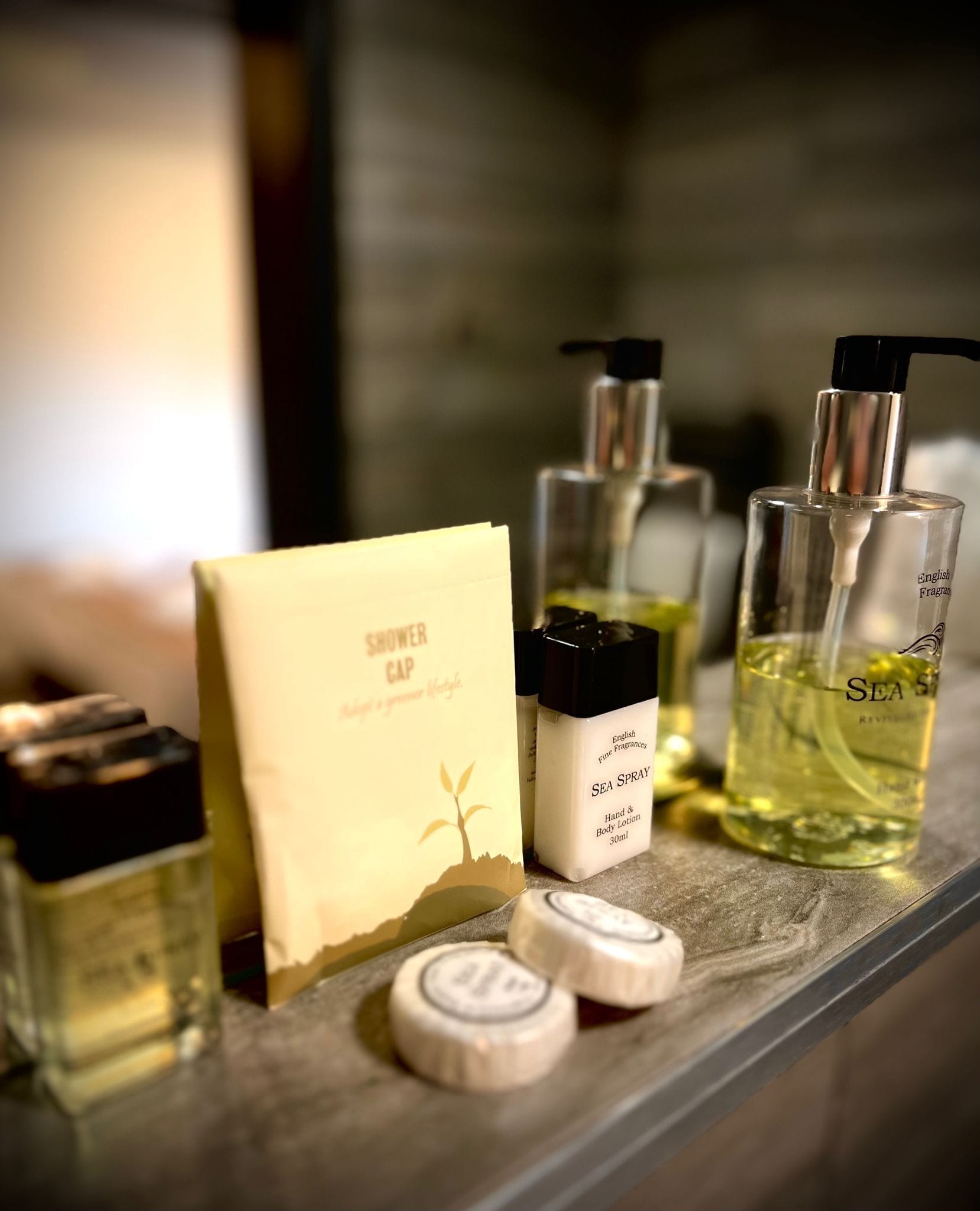 En badeværelseshylde med forskellige toiletartikler, herunder en brusehuvedæksel, hånd- og bodylotion samt flasker med håndsæbe og bodylotion.