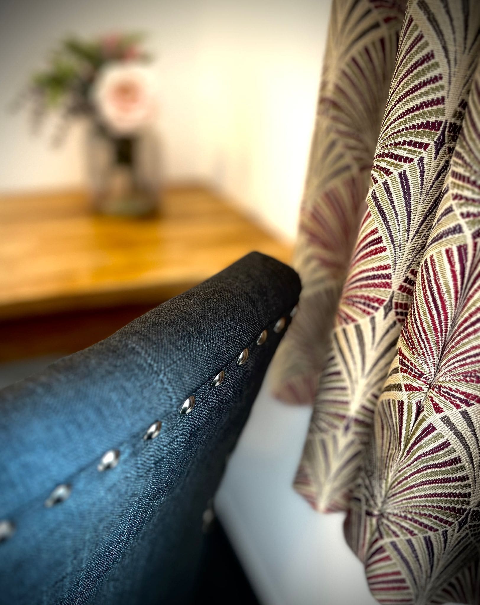 A close-up of a chair with a dark fabric and metal studs, and a patterned fabric draped over it.