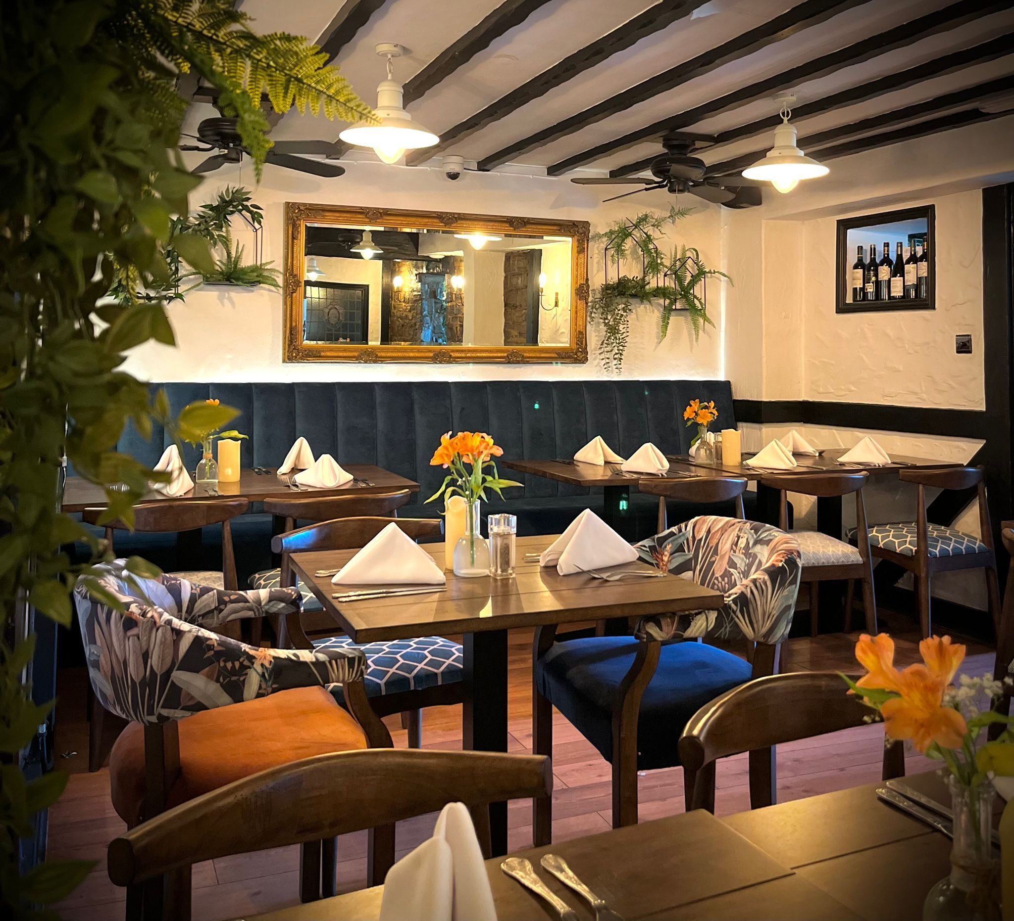 A restaurant interior with wooden tables, blue cushioned chairs, and a mirror above the bar area.