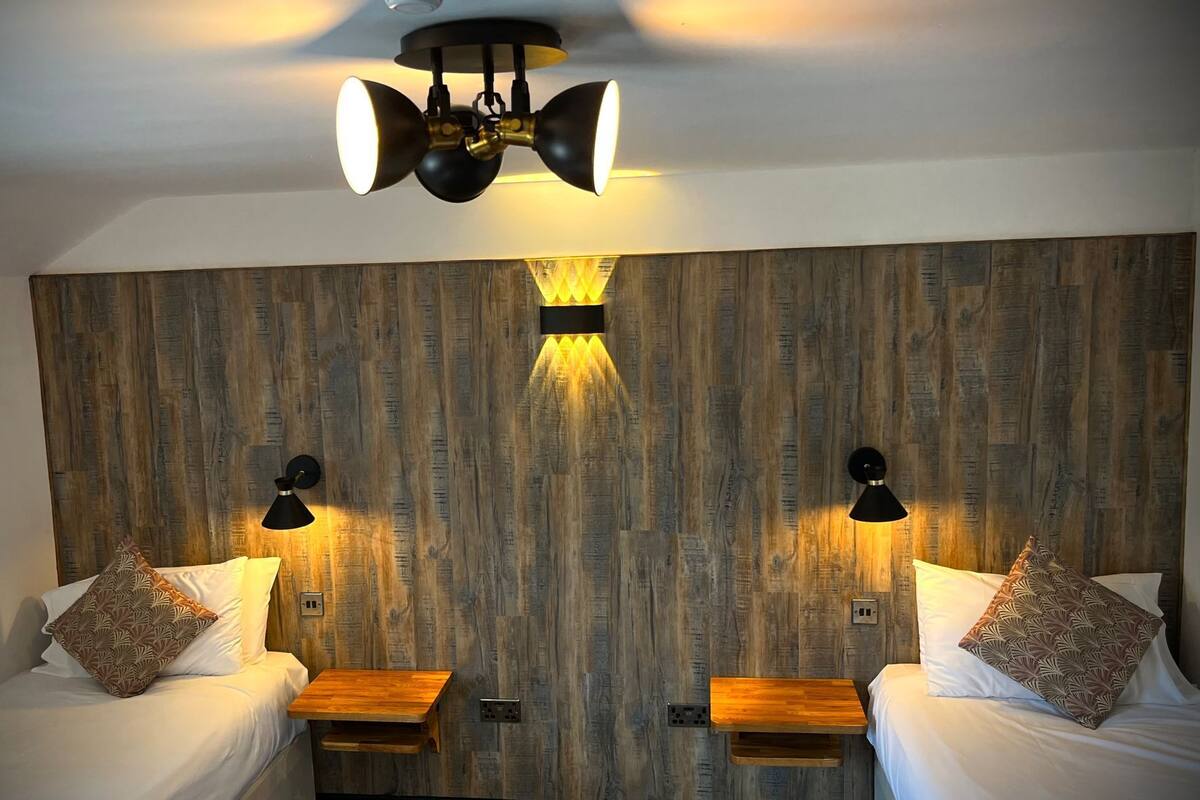 A room with two beds, wooden headboard, and three wall-mounted lights.