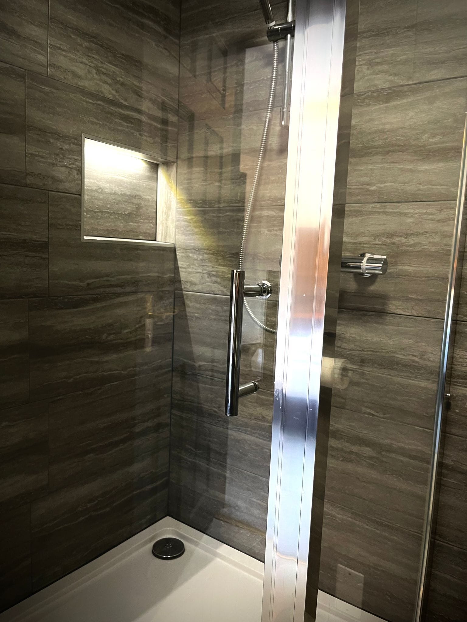 Un box de ducha moderno con puerta de cristal, un cabezal de ducha manual y un panel de control.