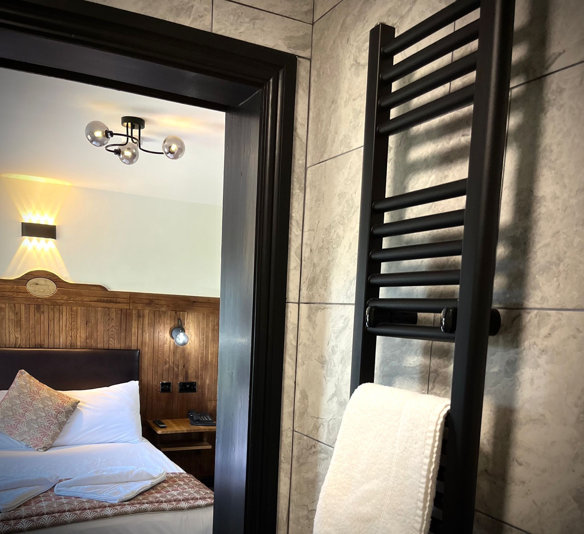 A hotel room with a bed, a bedside table, a lamp, and a towel rack.