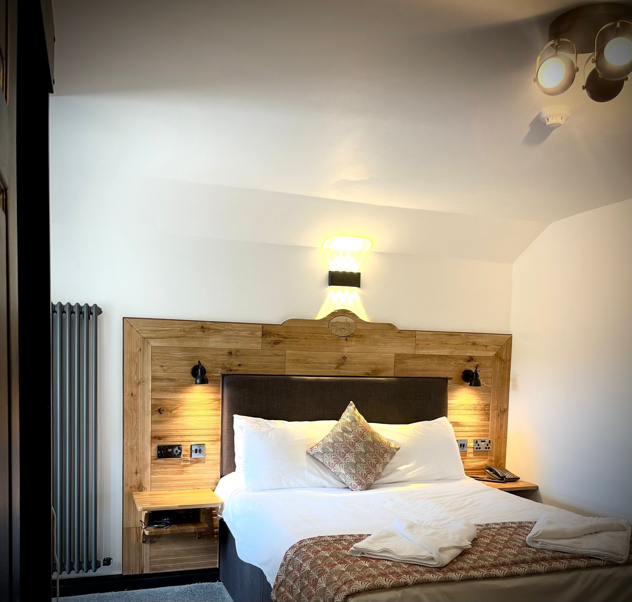 A modern bedroom with a wooden headboard, a bedside table with a lamp, and a telephone.