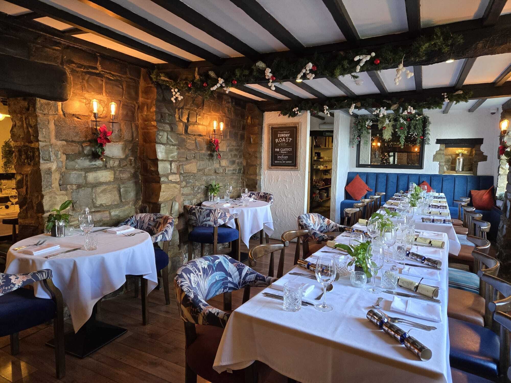 A restaurant with stone walls, wooden beams, and tables set for dining.