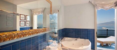 Une salle de bain dotée d’une grande baignoire, d’une douche à parois de verre et offrant une vue sur la mer depuis un balcon.