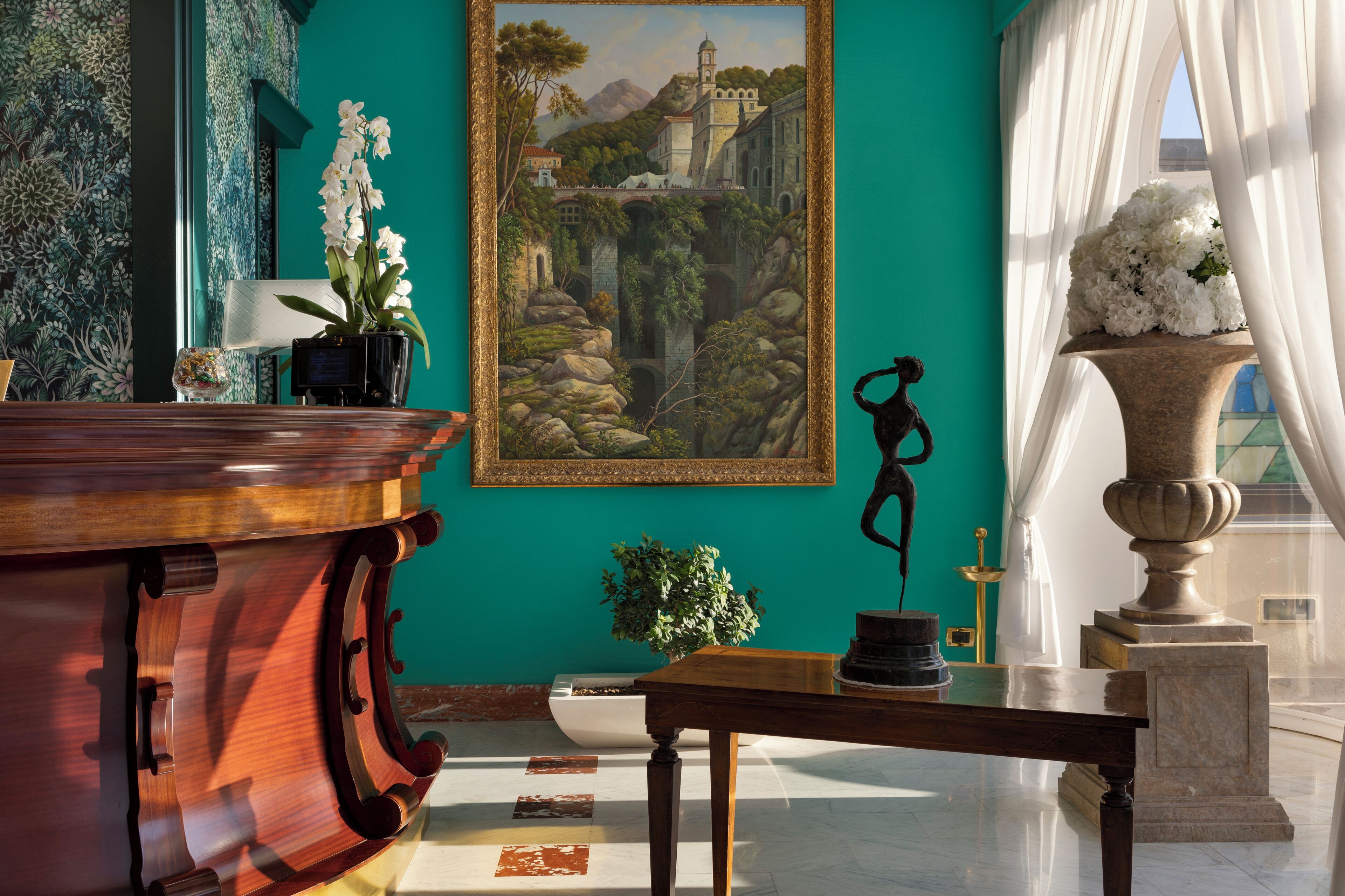 Una habitación con una mesa de madera, un cuadro enmarco, una planta en maceta y una estatua.