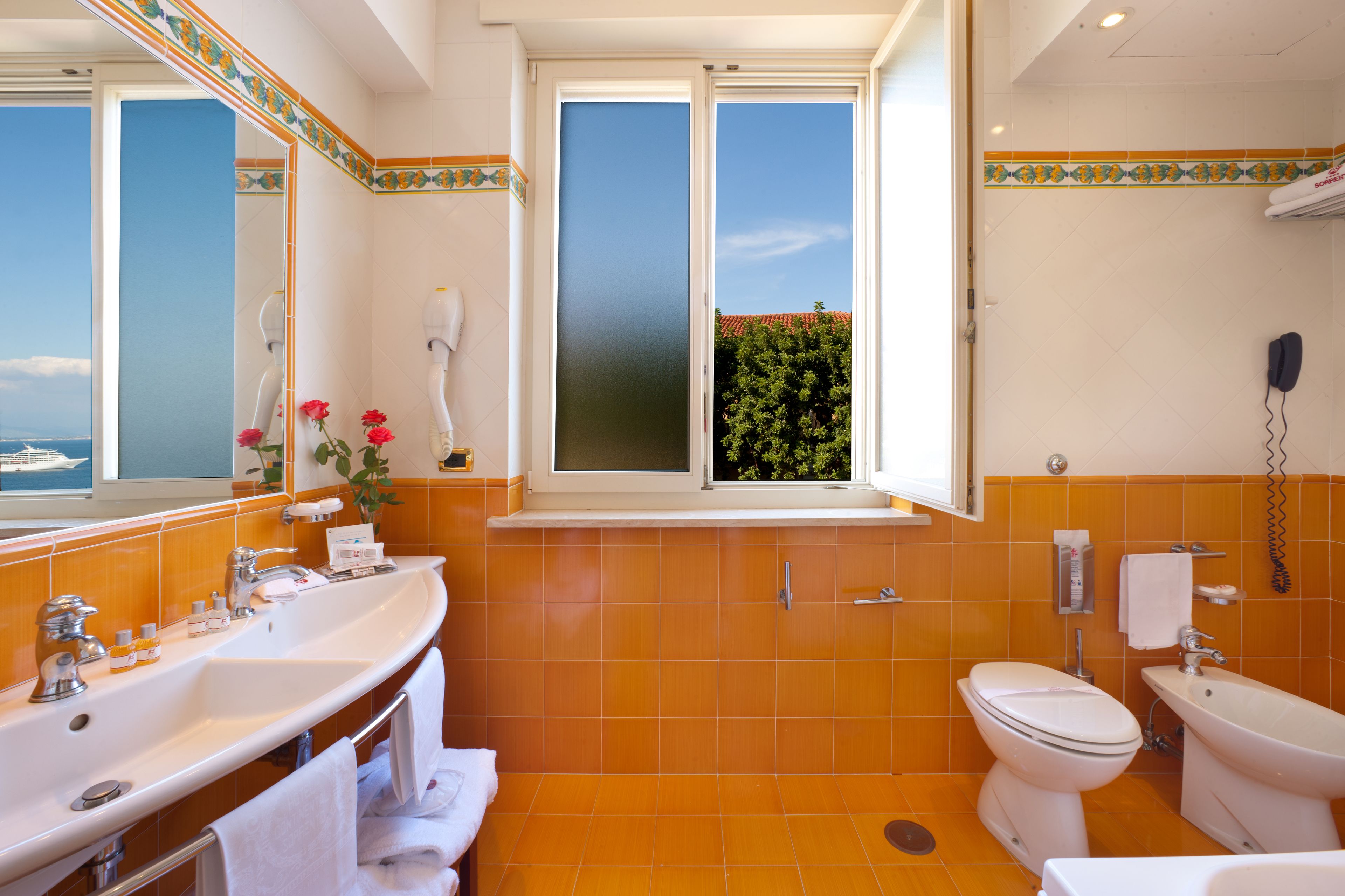 A bathroom with a large window, a bathtub, a toilet, and a sink.