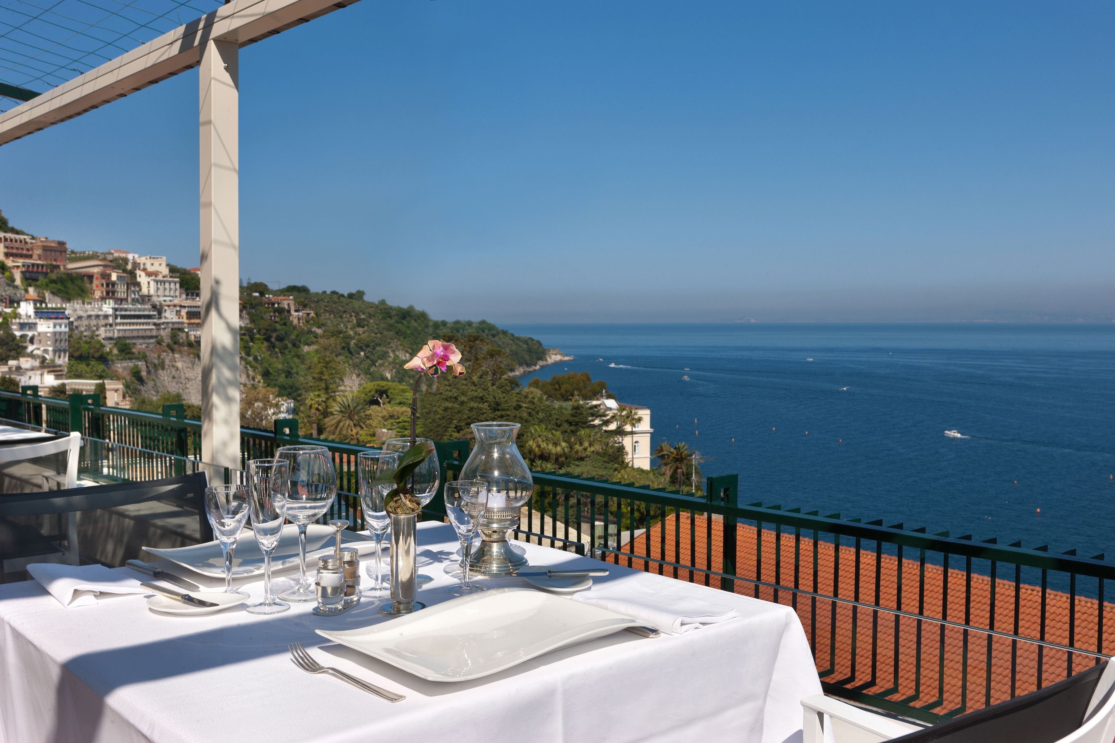 A table set for dining with a view of the sea and buildings in the background.