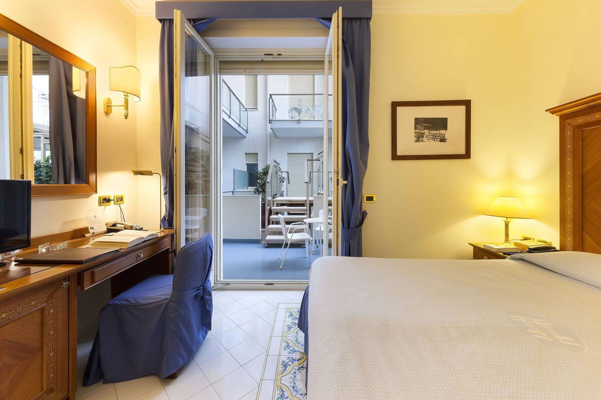 Una camera d'albergo con un letto, una scrivania, una sedia e vista su un balcone e uno spazio all'aperto.