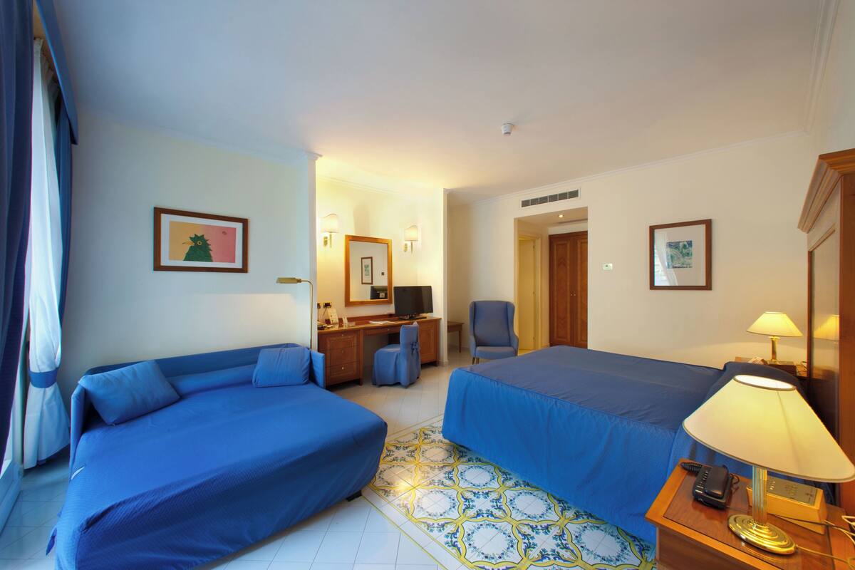 Una camera d'albergo con due letti, una scrivania, una sedia, una lampada e un telefono.