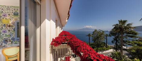 Ein Balkon mit roten Blumen, Blick auf das Meer und ein Berg in der Ferne.
