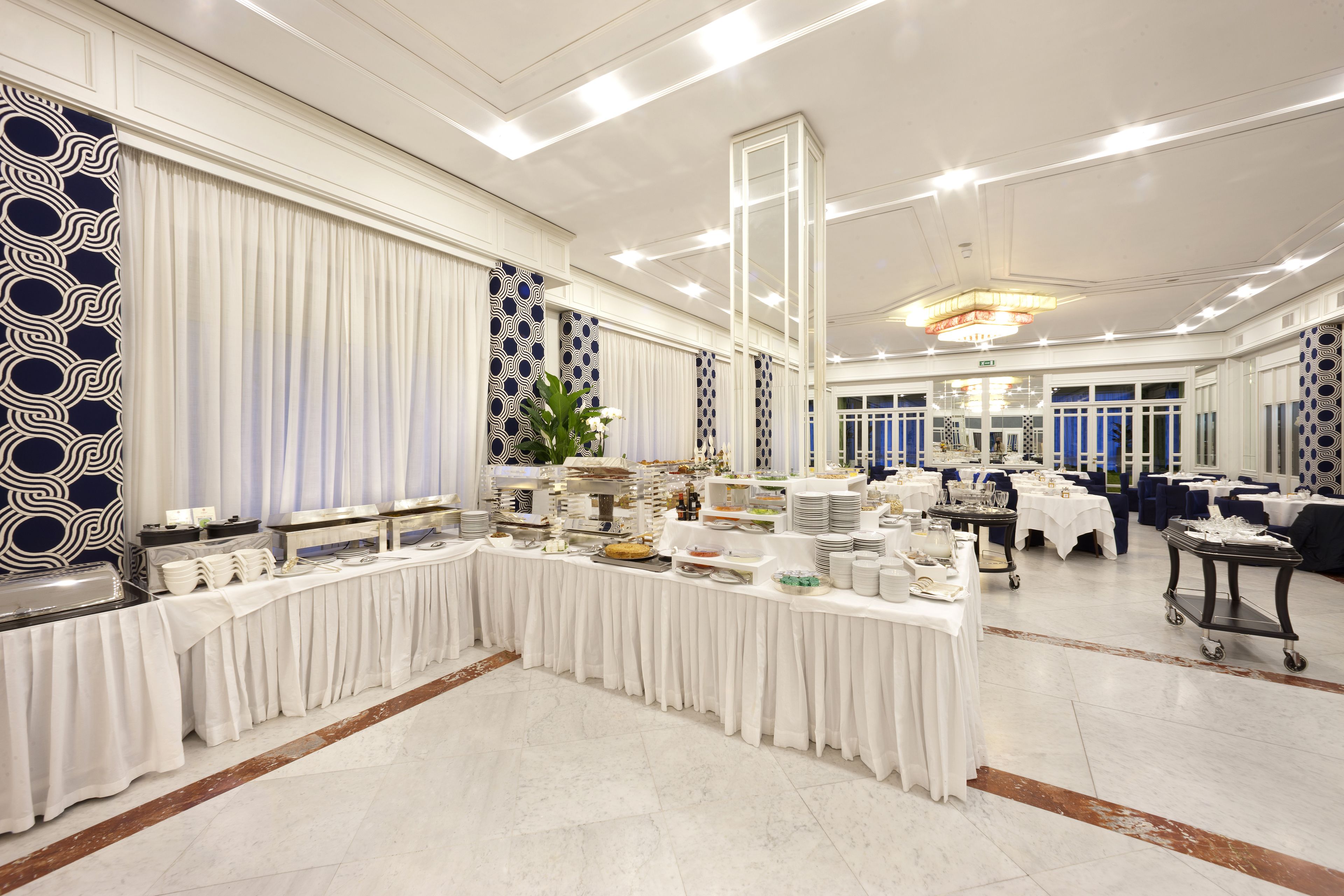 Un salón de banquetes con una larga mesa dispuesta para un bufé, rodeado de sillas y mesas.