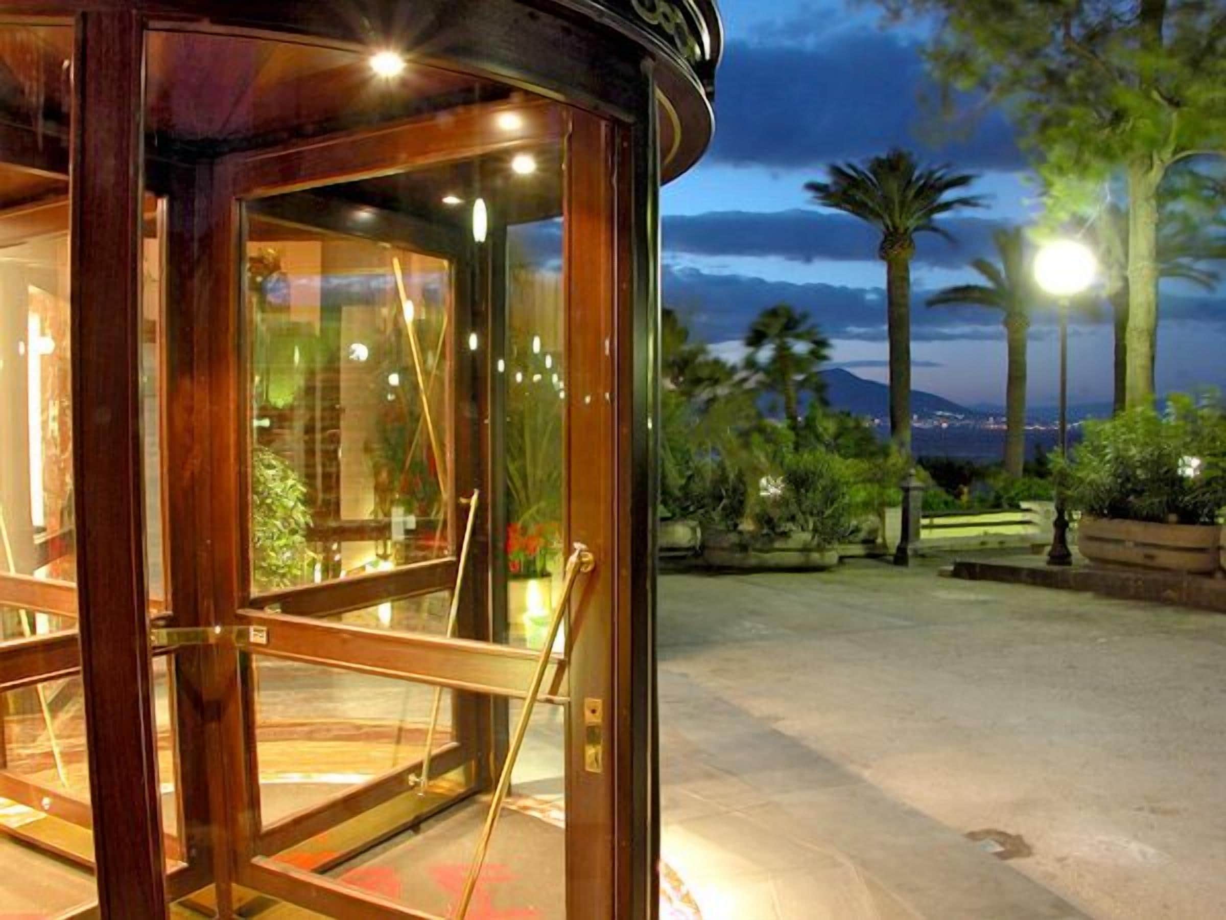 A wooden revolving door leading to a glass door with a view of palm trees and a distant cityscape.