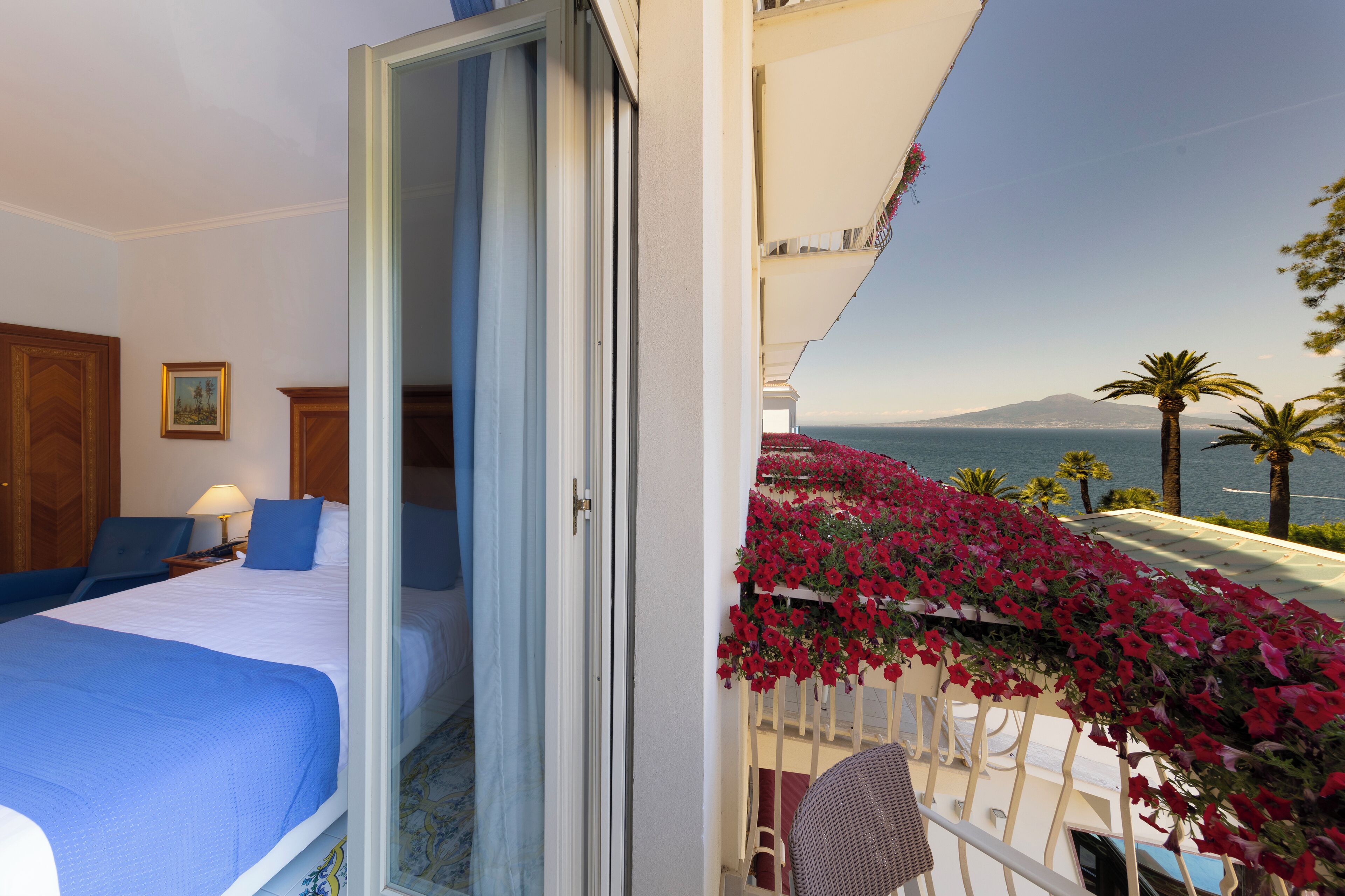 A hotel room with a bed, a chair, a nightstand, and a view of the sea and mountains.