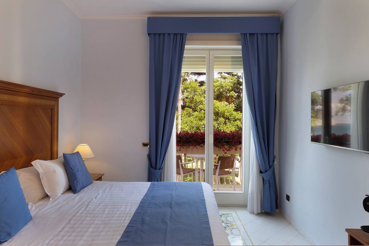 Una camera da letto con un letto, un comodino, una TV e vista su una zona esterna con tavolo e sedie.