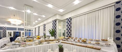 Un salón de banquetes con una larga mesa dispuesta para un evento formal, que incluye una variedad de platos y un arreglo floral central.