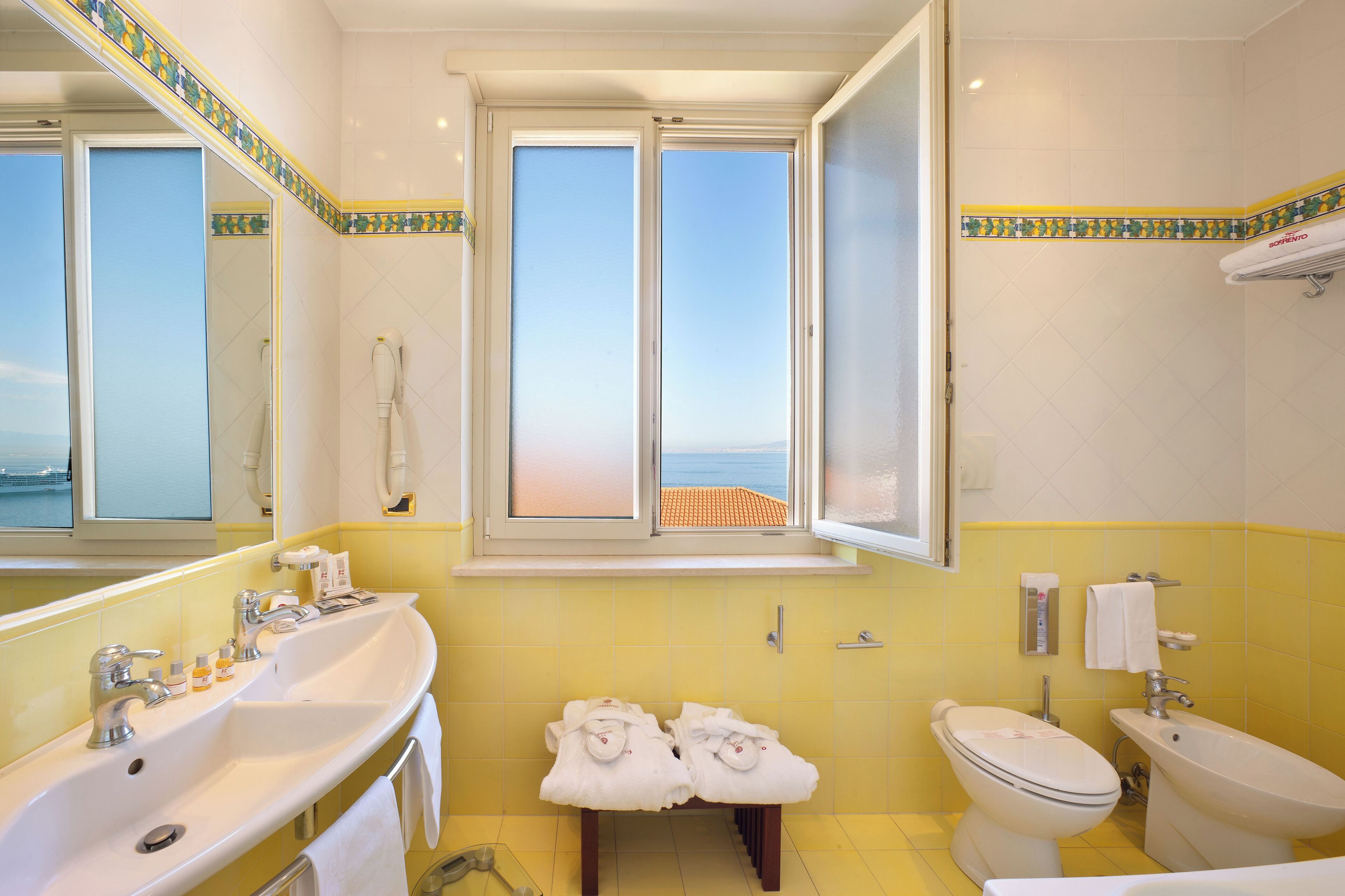 A bathroom with a large window, a sink, a toilet, and a bidet.