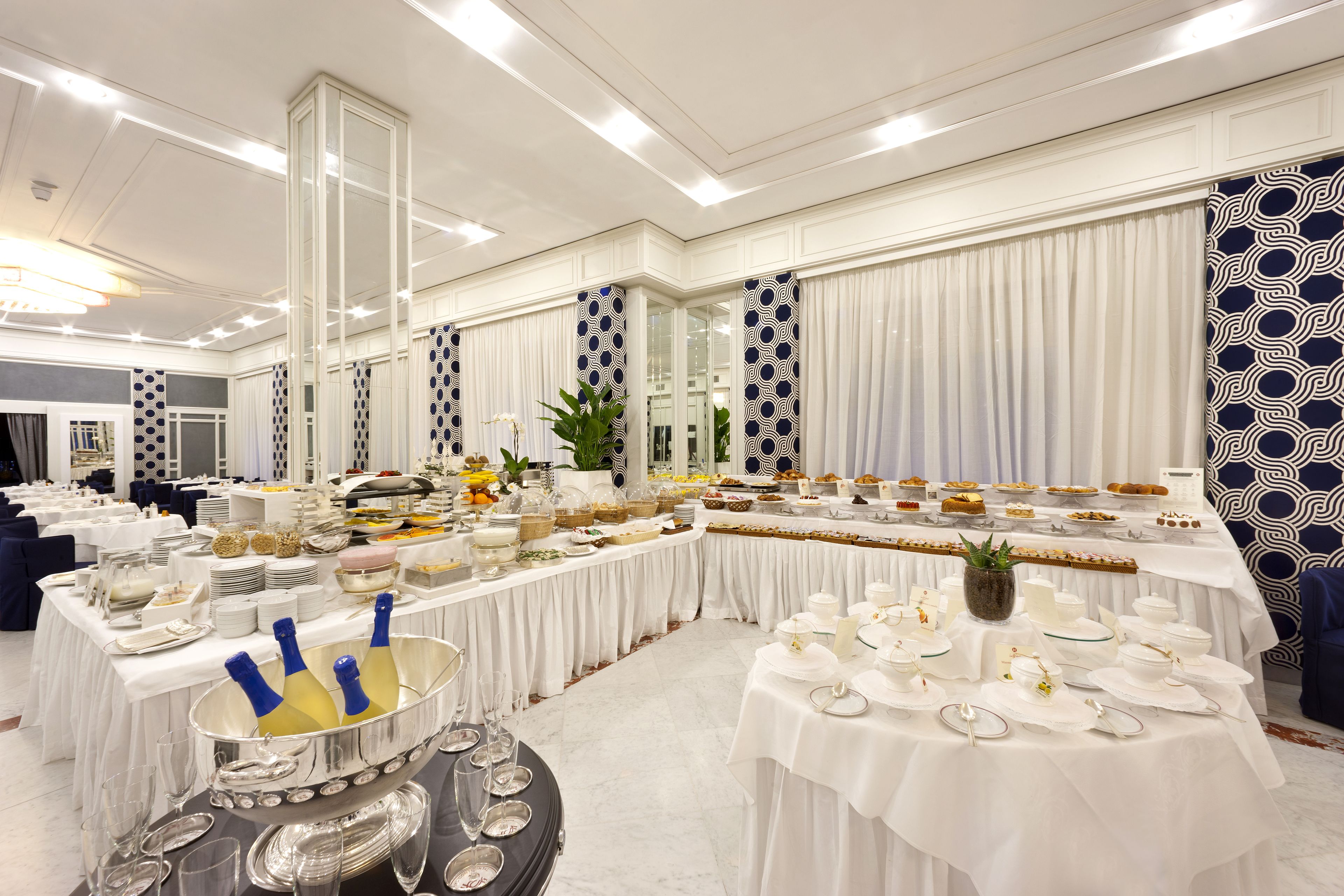 A banquet hall with tables set for a formal event, featuring white tablecloths, silverware, and a variety of dishes.