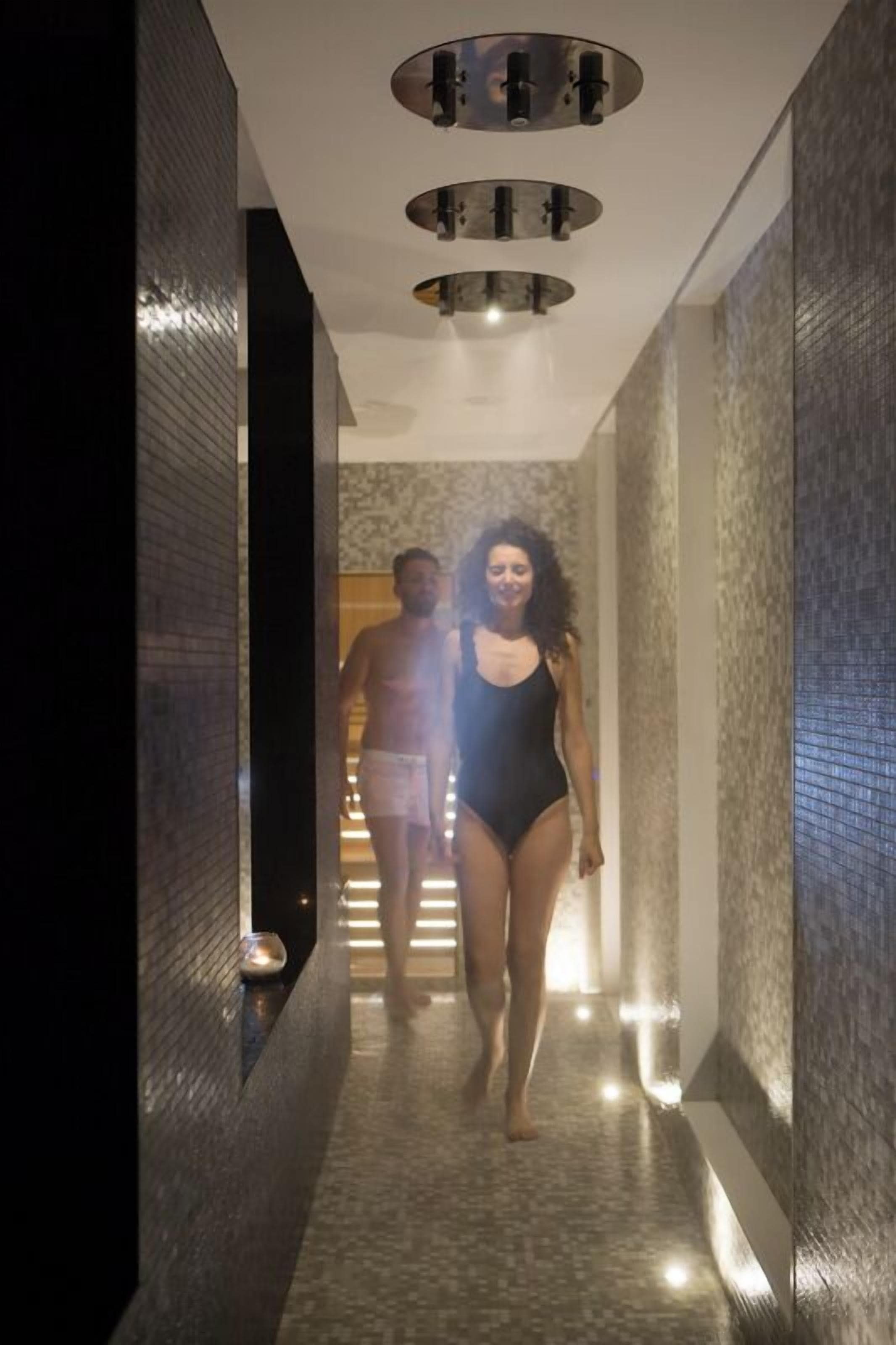 Un couloir moderne avec un mur texturé et un plafond orné de luminaires circulaires.