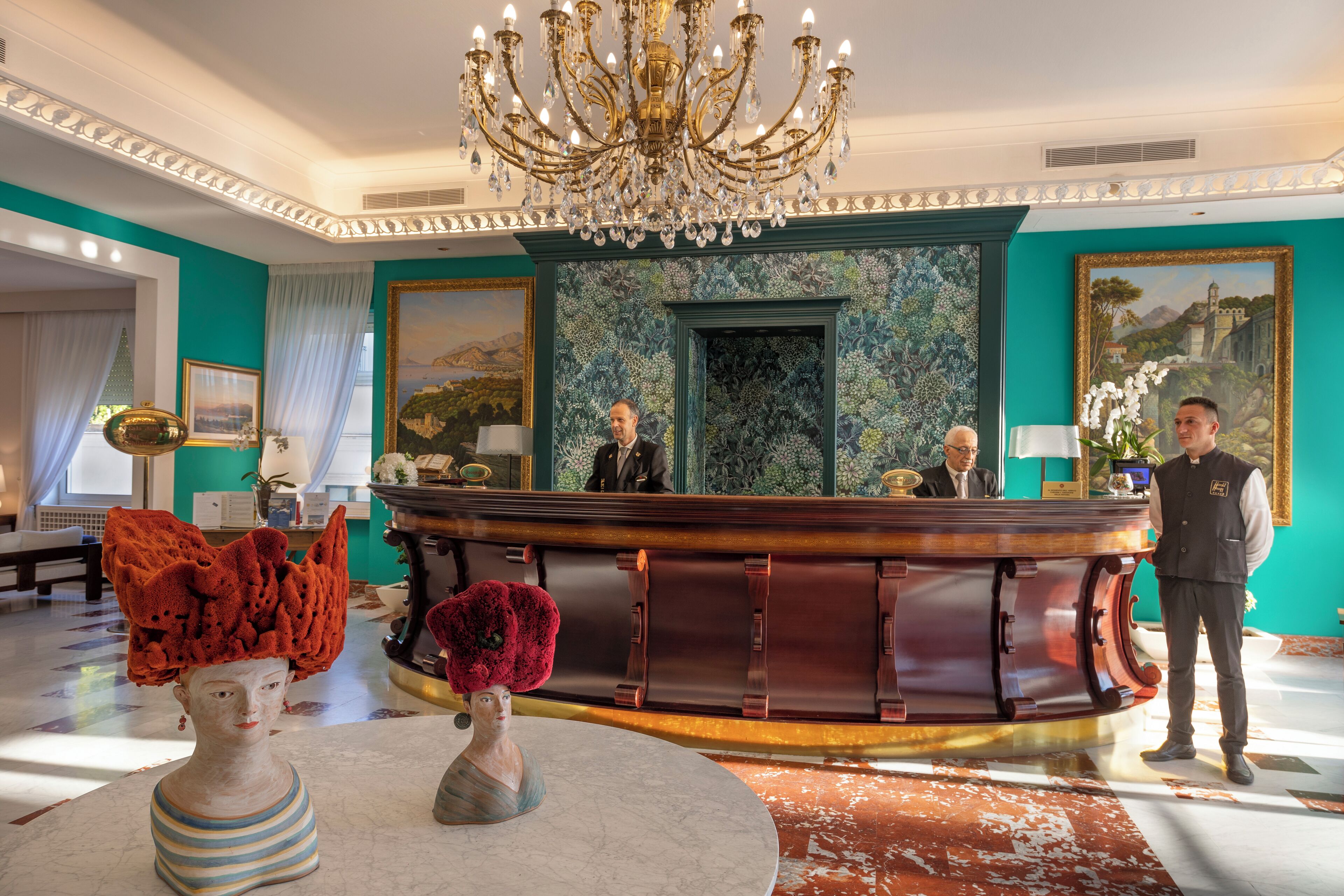 A lobby with a reception desk, a chandelier, and a large painting on the wall.