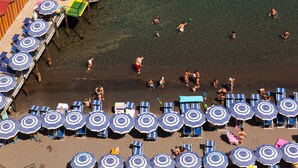 Un muelle con hileras de sombrillas azules y blancas y sillas, que se extiende hacia aguas azules y cristalinas.