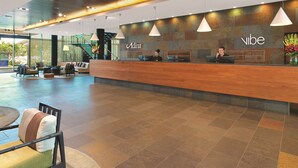Et moderne receptionsområde med en træreception, to receptionistansatte og et siddeområde med stole og sofa.