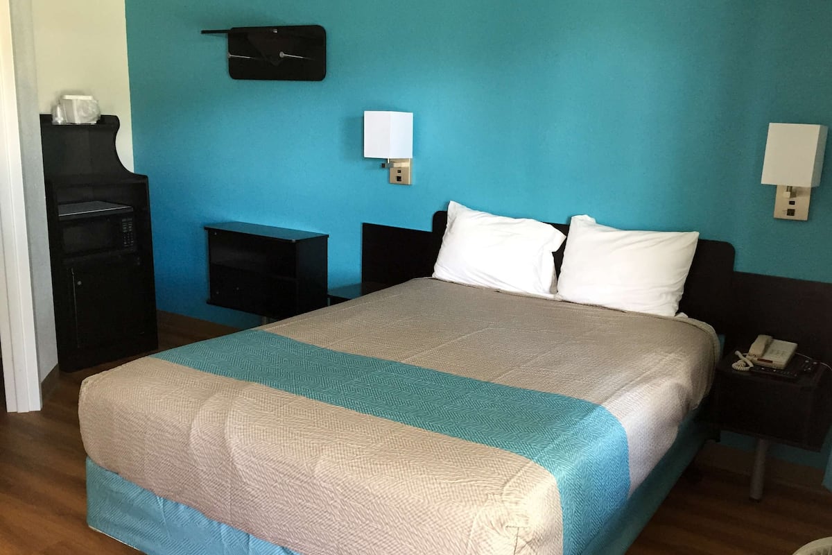 Une chambre d’hôtel équipée d’un lit, d’un bureau, d’un téléphone et d’une lampe fixée au mur.