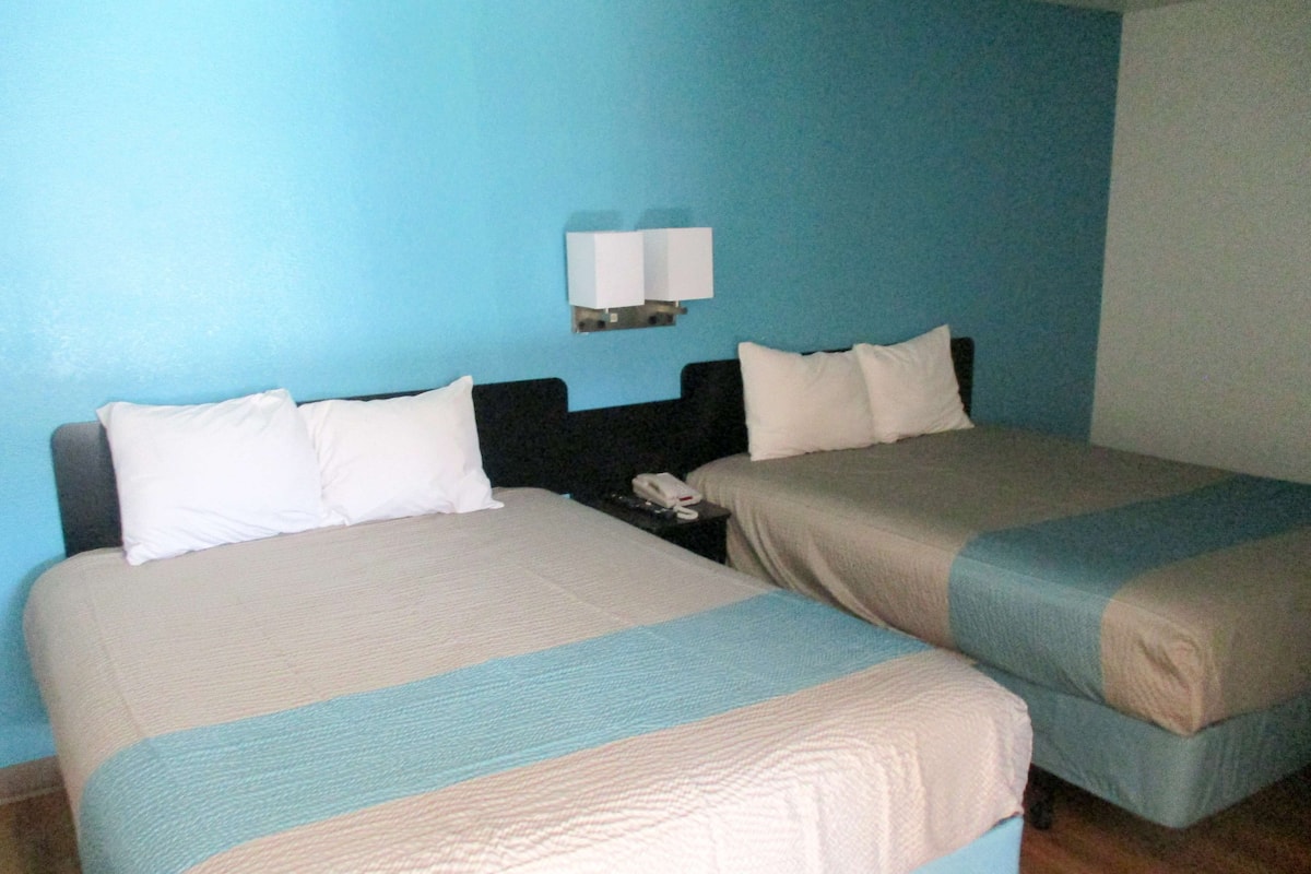 Une chambre d’hôtel avec deux lits, une table de chevet avec un téléphone et une lampe fixée au mur.