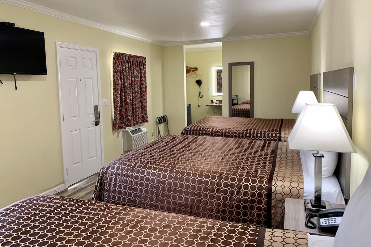 A hotel room with two beds, a TV, a desk with a lamp, and a mirror.