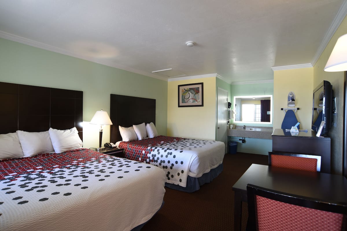 A hotel room with two beds, a desk, a chair, a mirror, and a bathroom visible through an open door.