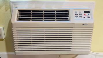 A white portable air conditioner with a control panel, placed against a wall with a patterned curtain.