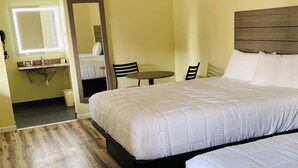 Habitación de hotel con dos camas, suelo de madera, una mesita con sillas, un espejo y un lavamanos.