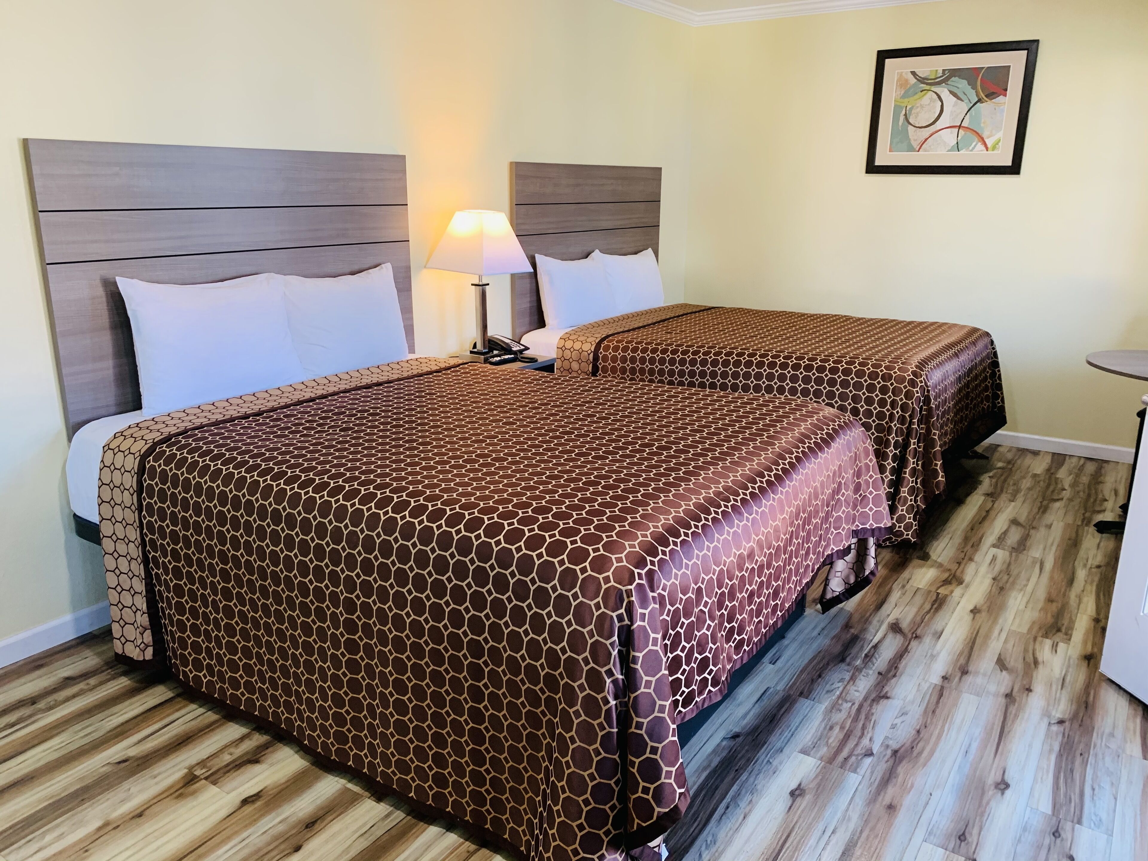 A hotel room with two beds, each with a patterned bedspread, a bedside lamp, and a framed picture on the wall.