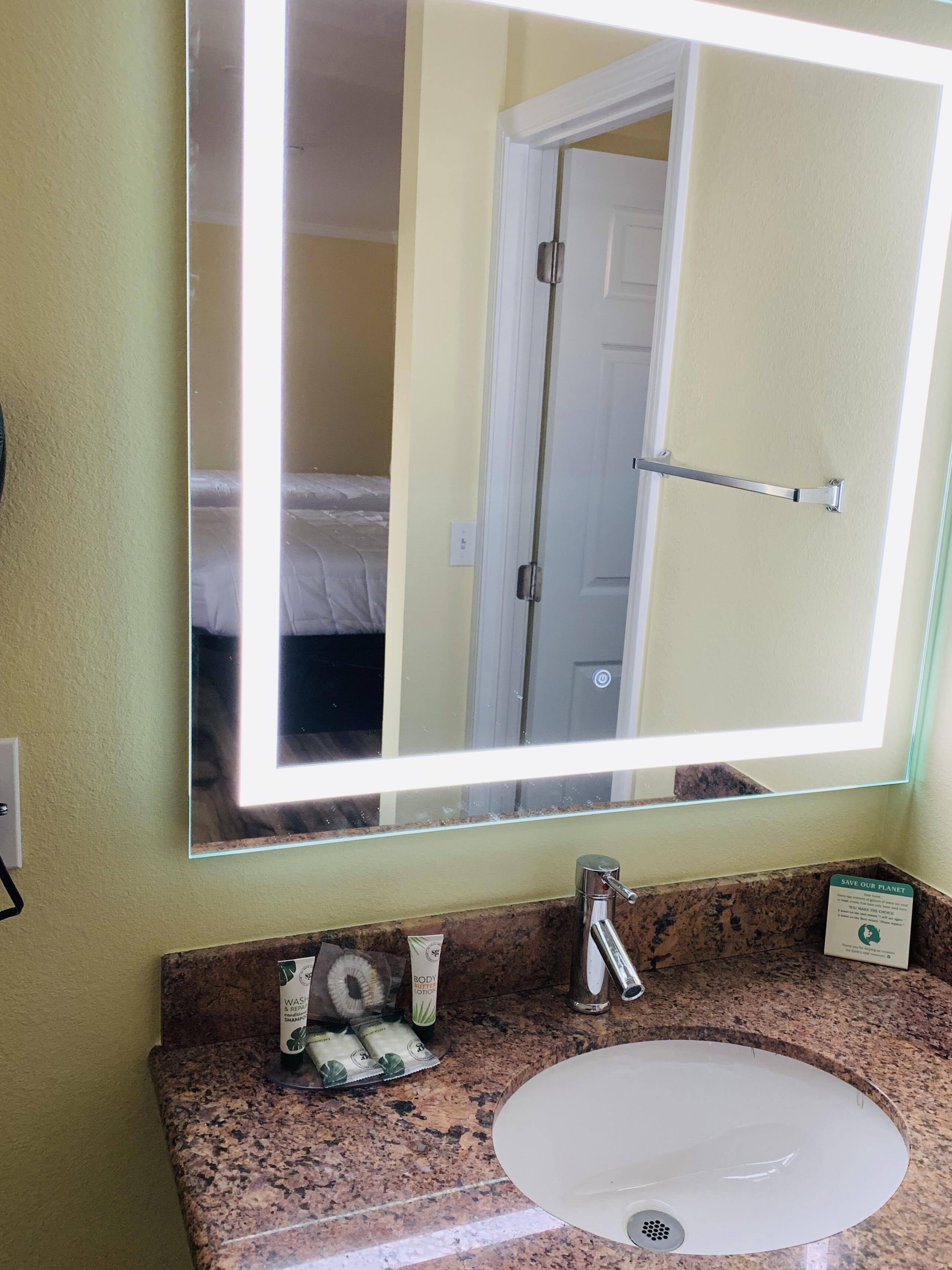 A bathroom with a large mirror, a sink, and toiletries on the counter.