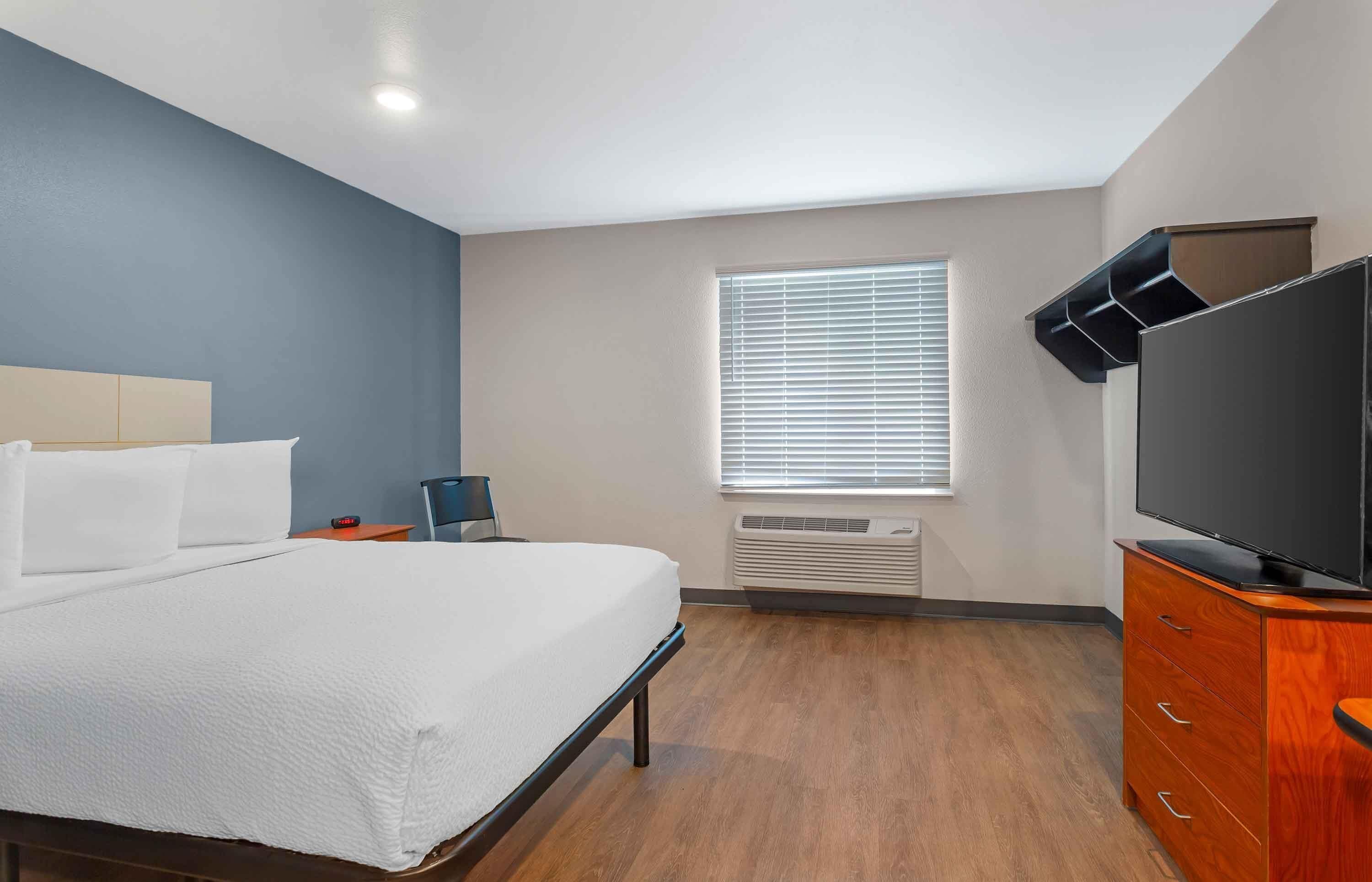 Une chambre d’hôtel équipée d’un lit, d’une télévision, d’un radiateur et d’une fenêtre avec des stores.